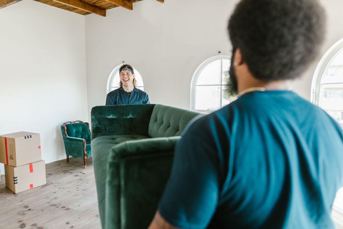 Twee leveranciers dragen een groene fluwelen zetel een lichte kamer binnen