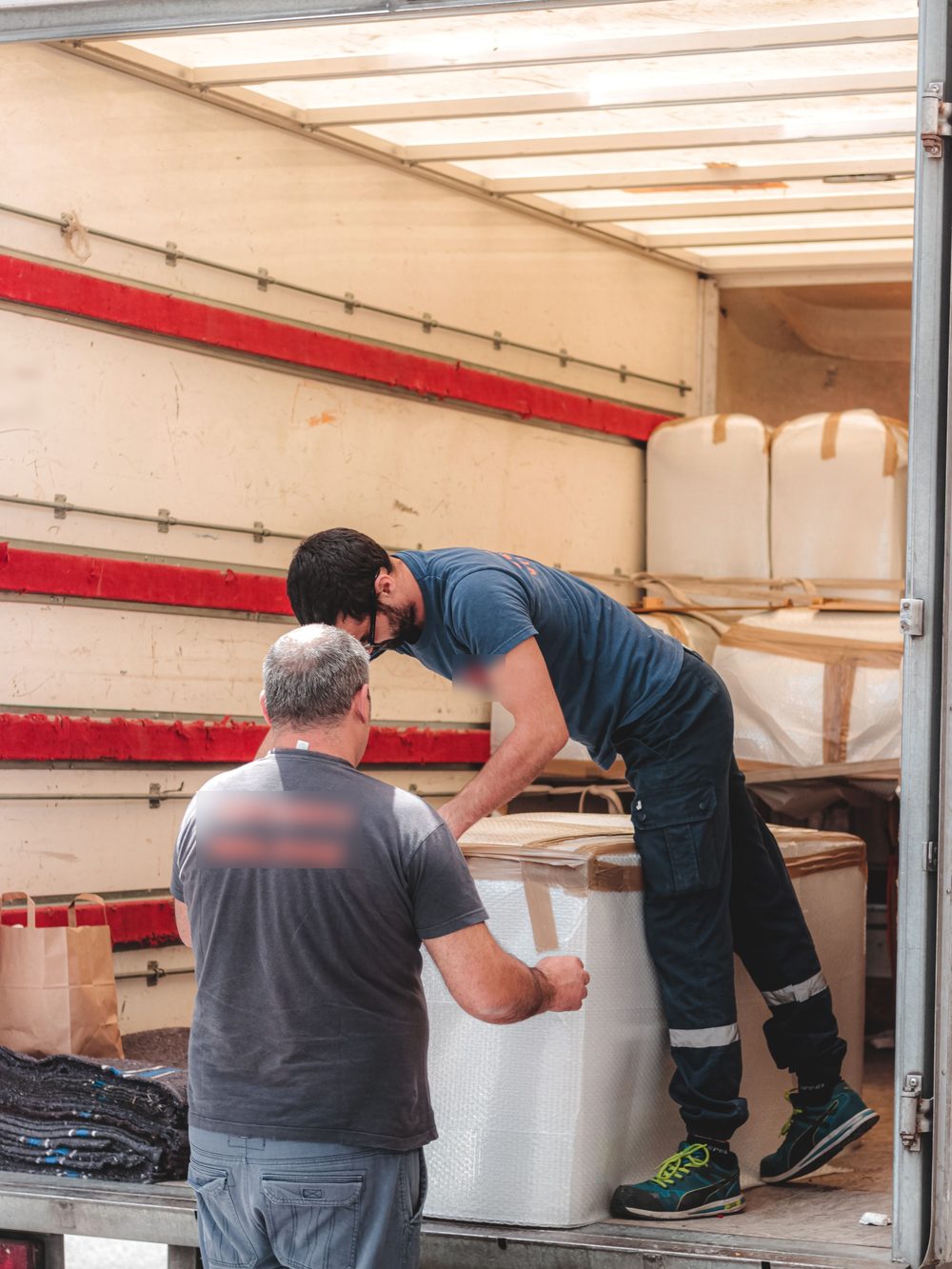 Twee mannen laden een ingepakt meubel in de laadruimte van een vrachtwagen